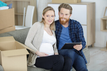 pregnant couple using tablet surrounded by boxes at home