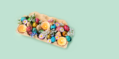 carton box with colorful eggs, diy candles in eggs shells, flowers on green background. festive spring season. table decor for Easter holiday, Ostara sabbat.  flat lay. banner. copy space - obrazy, fototapety, plakaty
