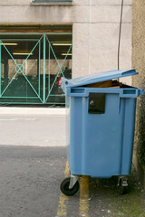 Naklejka premium Medium size wheelie waste bin in a street alley. Waste management industry in a city. Removing town rubbish. Keeping environment clean.