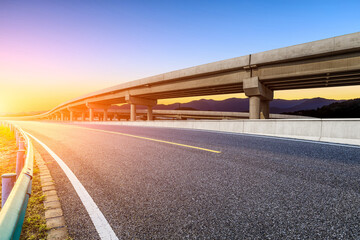Asphalt road and bridge with mountain background at sunset