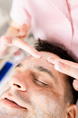 Beautician doing face treatment in beauty salon to a man.