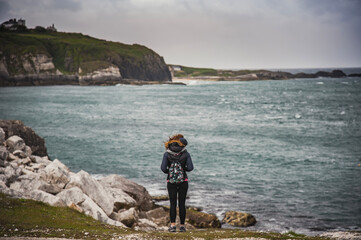 Back view of a woman taking a break while hiking to admire the dramatic cliffs and Irish gloomy...