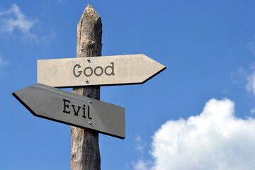 Good and evil - wooden signpost with two arrows, sky with clouds