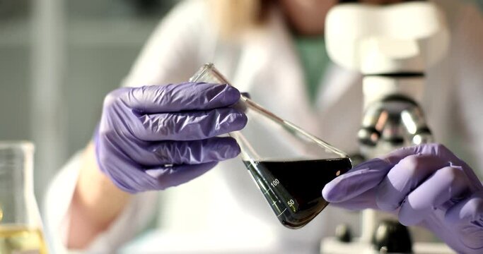 The hands chemist hold a sample of black oil in a flask