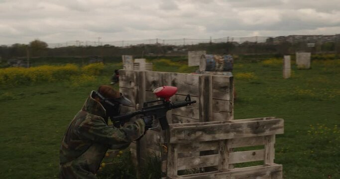 A woman sheltered behind some wooden pallets in a paintball field under a cloudy sky