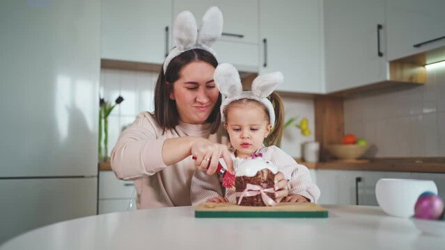 Beautiful mother and daughter are cutting a delicious Easter cake. Happy Easter.