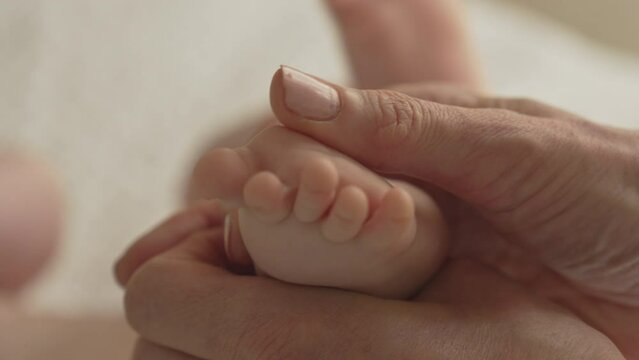 Closeup newborn baby feet and fingers, mom massages circles with hands