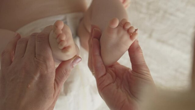 newborn baby feet and toes, mom massages with both hands, white bedsheets
