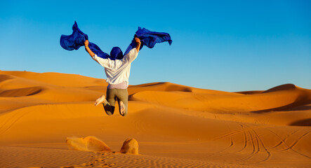 Woman with blue turban jumping in the desert- happiness,  travel,  freedom concept