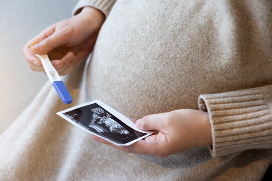 A pregnant woman is sitting with an ultrasound picture and a pregnancy test