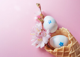 Close up of easter eggs, cherry blossom flowers, waffle cone on pink background with copy space