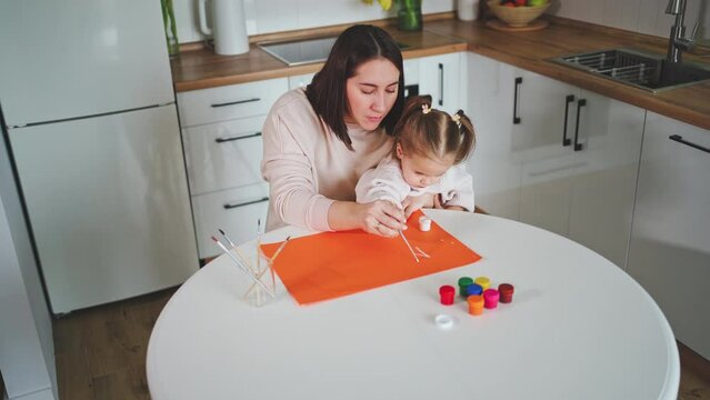 Beautiful daughter and mother draw a greeting card together in a cozy white kitchen. Mother's Day