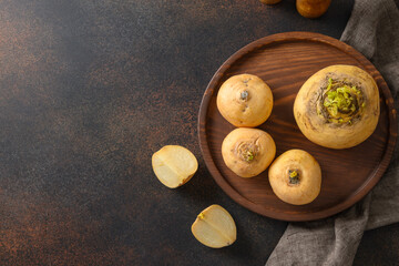 Fresh yellow turnip with stems in wooden tray on brown background. Top view. Copy space. Autumn...