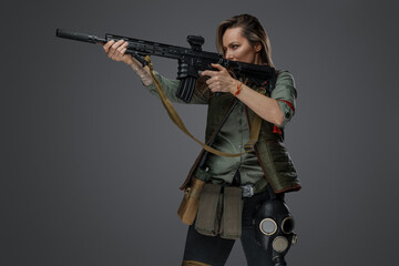 Portrait of military woman with rifle looking to side isolated on grey background.