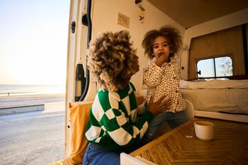 young black woman with fizzy hair spending time with her daughter in a camper van in a clear sprint...