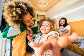 young interracial family spending quality time together with their daughter, who has a lot of fun in a bright camper van