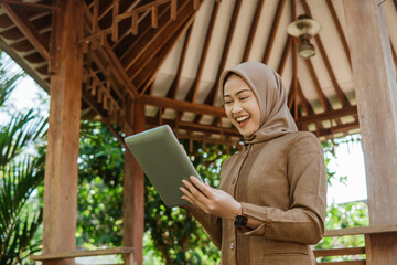 happy young female teacher in hijab using a pad against gazebo background