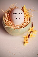 Wesoła pisanka na Wielkanoc - jajko z buźką w gniazdku. Symbol świąt wielkiej nocy i gałązka forsycji - obrazy, fototapety, plakaty
