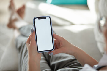 Mock up white screen blank mobile phone in woman hands holding lying on the sofa Back view