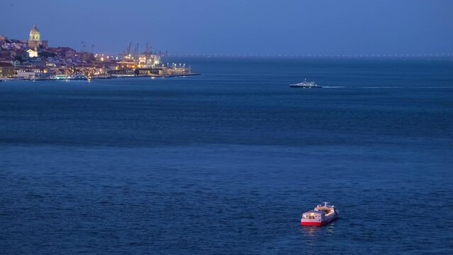 Night view of Lisbon over Tagus river from Almada with ferry and tourist boat in evening twilight. Lisbon, Portugal