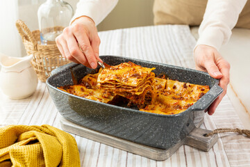 Woman hands serving or plating  homemade lasagne made with meat bolognese ragu sauce, bechamel and...