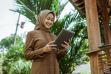 asian female teacher in hijab using a tablet standing in park