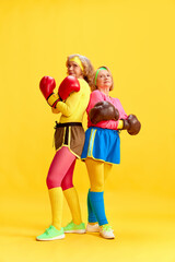 Active lifestyle. Elderly sportive women in colorful uniform posing in boxing gloves against yellow...