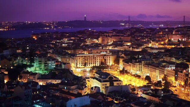 Night view of Lisbon city famous view from Miradouro da Senhora do Monte tourist viewpoint over Alfama old district, 25th of April Bridge in the evening twilight. Lisbon, Portugal. Camera pan