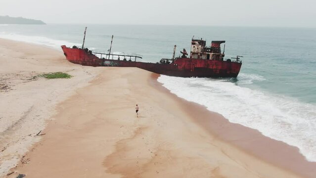 a tourist walking towards an abandoned shipwreck on the west african coast in Robertsport, Liberia