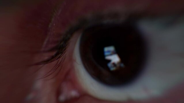 Scrolling smartphone feed with tech news. Man's eye watching smartphone screen while scrolling through online news and information. Online information and fake news, closeup macro detail of an eye.