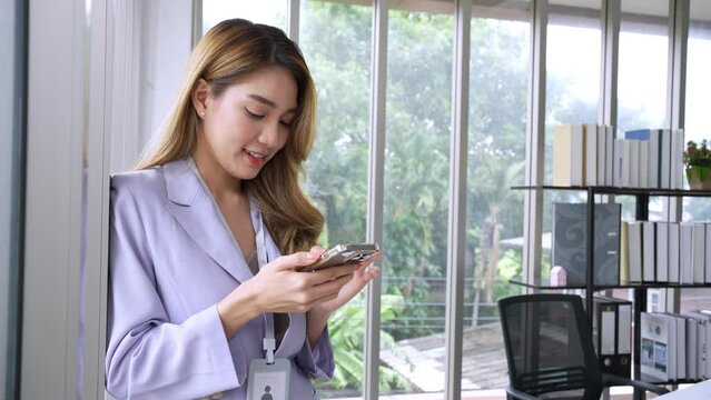Portrait of smart confidence Asian female startup entrepreneur uses phone and Internet technology, SME online store social e-commerce sale page service web support. Surf the internet or shop online