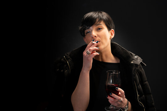 A young woman drinks wine and smokes a cigarette
