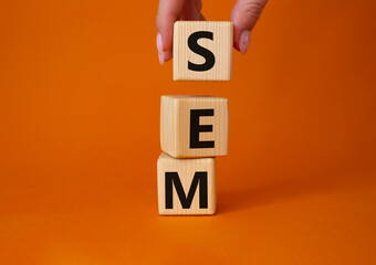 SEM - Search Engine Marketing symbol. Wooden cubes with words SEM. Businessman hand. Beautiful orange background. Business and SEM concept. Copy space.