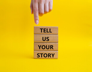 Tell us your story symbol. Concept words Tell us your story on wooden blocks. Beautiful yellow background. Businessman hand. Business and Tell us your story concept. Copy space.