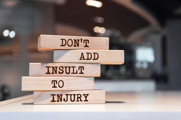 Wooden blocks with words 'Don't add insult to injury'. - obrazy, fototapety, plakaty