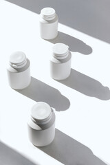 Minimal style composition made of white plastic bottles for supplement, vitamin, pills on sunlit background with shadow. Set of containers packaging with a cap. Pharmacy and medicine concept