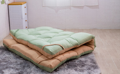 A side view of an orange and green mattress topper neatly folded on the floor in the middle of the...