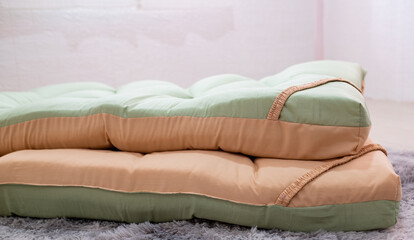 A side view of an orange and green half mattress topper neatly placed on the floor in the middle of the bedroom.
