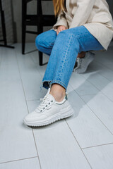 Female legs in white stylish sneakers. Casual women's fashion. Comfortable shoes for women. Women's comfortable summer shoes.