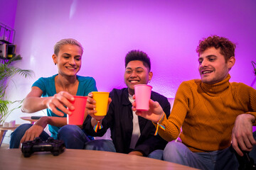 Group of young friends playing video games together on the sofa at home, toasting with glasses, young millennials