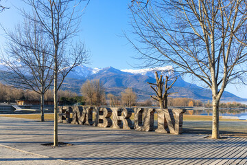 A scenics view of the Embrun, France lake with wooden sign, snowy mountains range in the background under a majestic blue sky