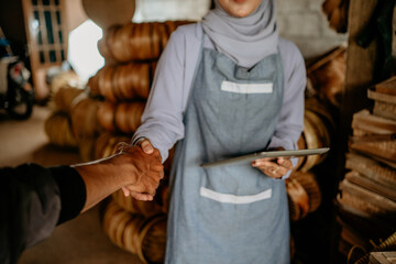 beautiful young muslim woman shake hand with customer in her woven bamboo product workshop