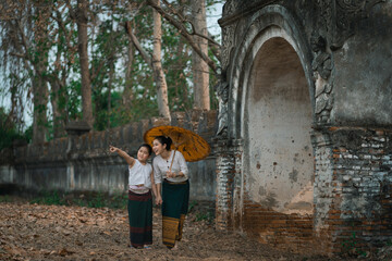 Mother and daughter dressed in traditional costumes with an umbrella walking at Wat Mon Jam Sil...