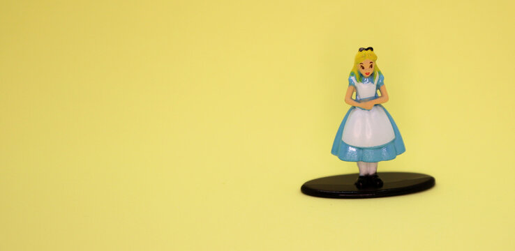Alice in Wonderland doll from the Walt Disney movie. Metallic figure on yellow background. Blonde girl in a light blue dress. Isolated. Character from Lewis Carroll's book.