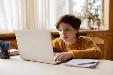 The child sits at home at his laptop on home schooling