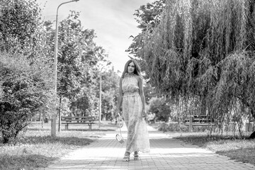 Black and white photo a cute girl in a summer dress with a floral print walks in a city dress. The background is a beautiful sky at sunset. Summer. Vacation concept