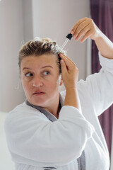  Woman applies oil to her hair with pipette. Beauty caring for scalp and hair. 