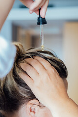 Woman applies oil to her hair with pipette. Beauty caring for scalp and hair.  - obrazy, fototapety, plakaty