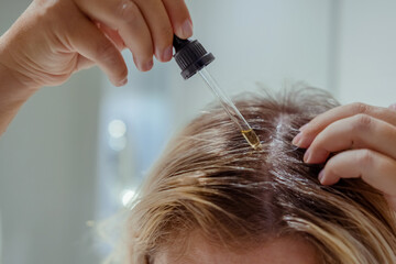  Woman applies oil to her hair with pipette. Beauty caring for scalp and hair.  - obrazy, fototapety, plakaty
