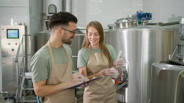 Man and woman working in craft brewery checking the pH value of the beer.